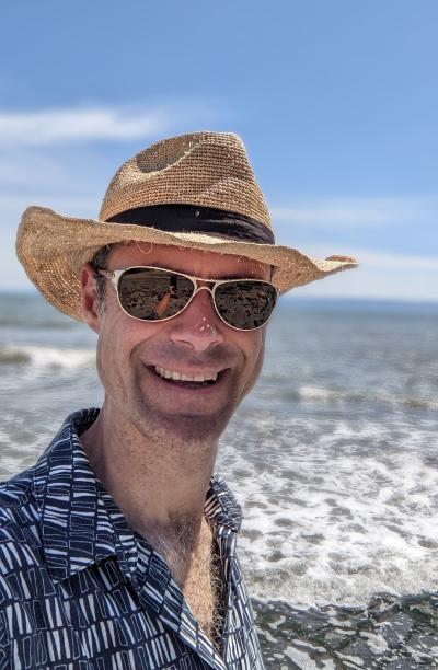 Drew on a beach, hat and sunglasses